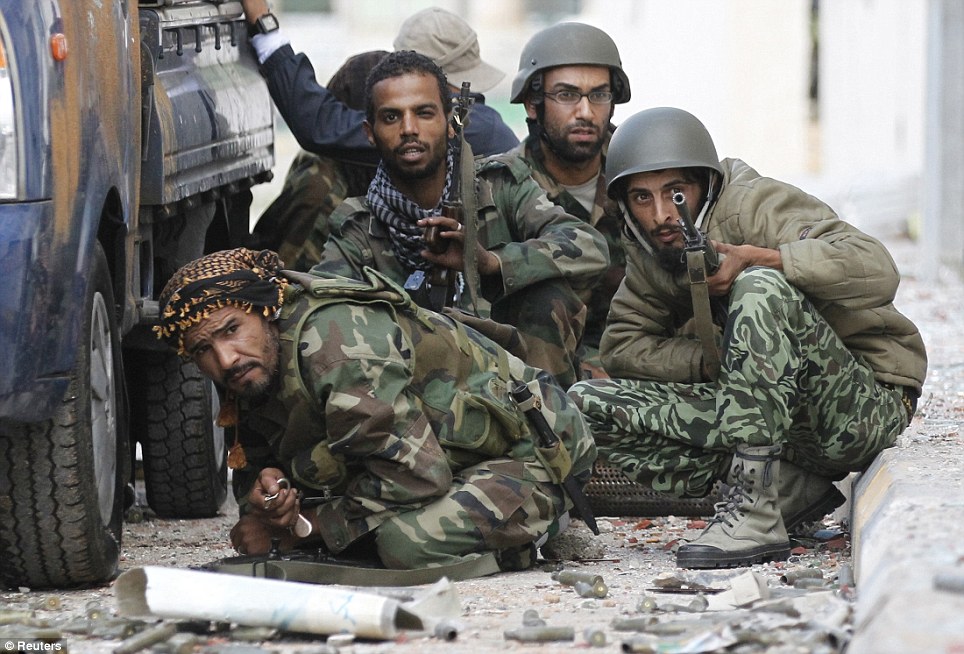 Taking cover: Anti-Gaddafi fighters crouch low behind one of their vehicles as heavy gunfire rains over their heads during the battle